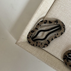 Macro shot of wave-edge leopard print hair clip with velvet texture on beige tray
