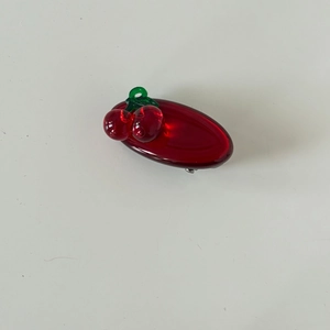 Detailed view of translucent red cherry hair clip with green leaves on silver metal