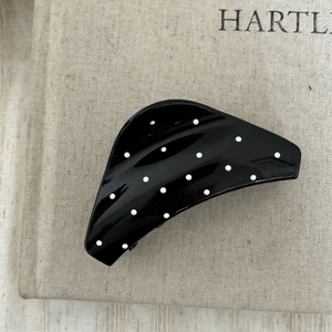 Pince à cheveux noire brillante à pois blancs sur un fond en tissu beige élégant