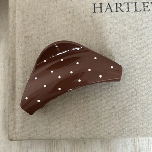 Détail d'une pince à cheveux marron à pois posée sur la couverture en lin d'un livre