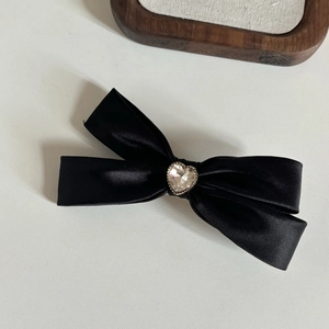 Dettaglio del fermaglio per capelli a fiocco nero in raso con strass a forma di cuore