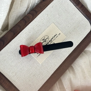 Elegant red acrylic bow hair clip on a natural wooden tray with a linen background