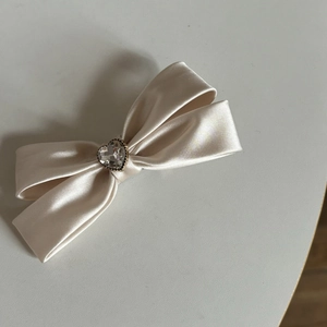 Dettaglio di un fermaglio a fiocco in raso crema con uno strass scintillante a cuore