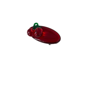 Translucent red cherry hair clip with green leaves on a glossy dark red oval base