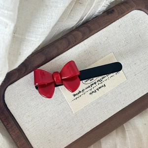 French style red bow hair clip with black duckbill grip on a decorative tray