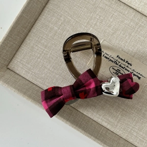 Detailed macro view of pink checkered bow hair clip with silver heart on beige fabric