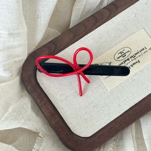 Close-up of red resin bow hair clip on a textured linen tray with a soft background