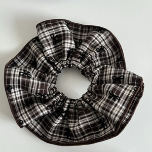 Close-up of brown plaid scrunchie with embroidered black bows and reinforced stitched edges