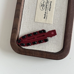 Detail of burgundy leather braided hair clip on a vintage linen and walnut tray