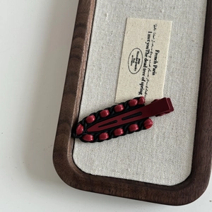 Macro detail of burgundy leather wrapped alloy hair clip on a premium wooden tray