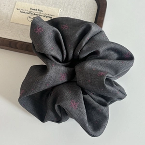 Close-up of charcoal grey twill fabric scrunchie with purple bow patterns and dots