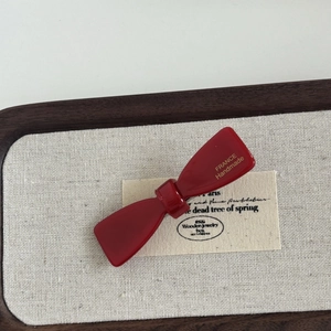 Detail of red acetate bow hair clip with gold France Handmade logo on a wooden tray