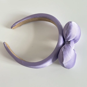 Close-up of a light purple padded satin headband with a large decorative bow and soft silk gloss