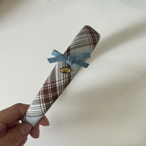 Detail of plaid headband with blue denim bow and gold oval love tag in hand