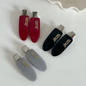 Dettaglio di fermagli per capelli in acetato rosso, nero e grigio con scritte dorate