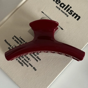 Gros plan d'une grande pince à cheveux rouge foncé brillante sur un fond de livre épuré