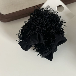 Détail d'un chouchou en peluche noir avec nœud en tissu sur carte d'emballage