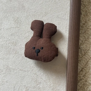 Detail of a brown fabric bear necklace pendant with minimalist stitched facial features