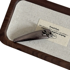 Gunmetal grey leather bow hair clip with vintage metallic finish on display tray