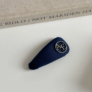 Detailed view of navy blue fabric hair clip with a round silver AE letter ornament