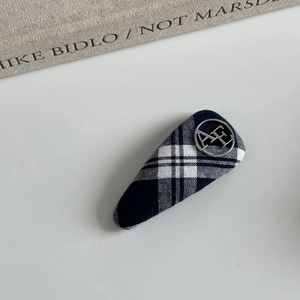 Close-up of blue plaid fabric hair clip with a round metal AF logo on white background