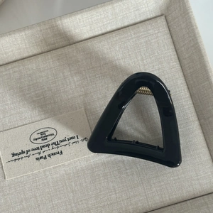 Macro detail of a glossy black triangular hair claw clip with a gold metal spring