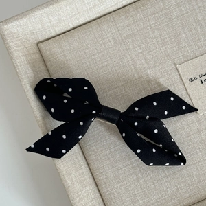 Vintage black and white polka dot bow hair claw clip on a beige textured display box
