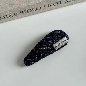 Detail of blue tweed hair clip with silver engraved metal plaque and white stitching