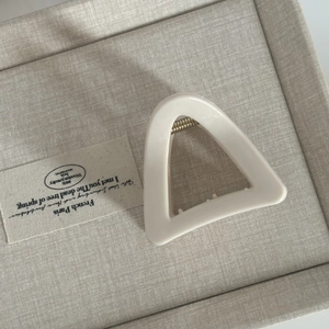 Close-up of a cream white triangular hair claw clip with golden metal spring detail