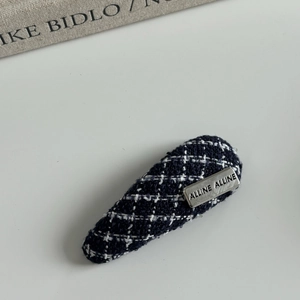 Detailed texture of blue tweed fabric hair clip with engraved silver metal tag