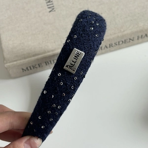 Detailed close-up of navy blue tweed headband with silver sequins and a metal logo plaque
