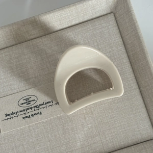 Minimalist cream white D-shaped resin hair claw clip resting on a textured fabric box