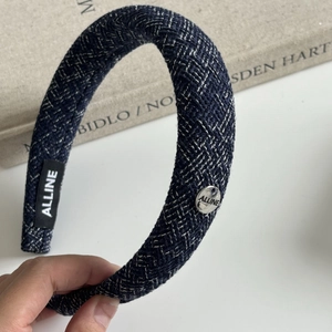 Detail of blue tweed headband with silver brand logo plate and rich fabric texture