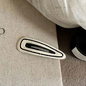 Detail of cream leather BB hair clip with black hand-stitched stripes and metal clasp