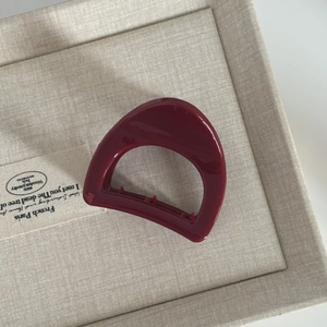 Detail view of the burgundy pumpkin hair claw with polished finish on beige fabric