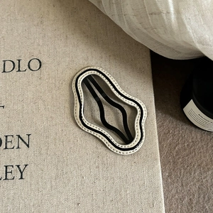 Close-up of wavy black and white hairpin with cream stitching on rustic linen background