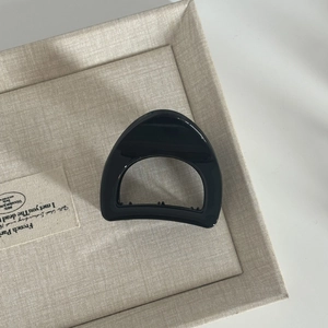 Macro shot of a glossy black hollowed-out hair claw clip on a textured beige tray