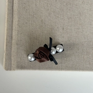 Detail of brown satin rose hair clip with white pearls and black ribbon bow on linen