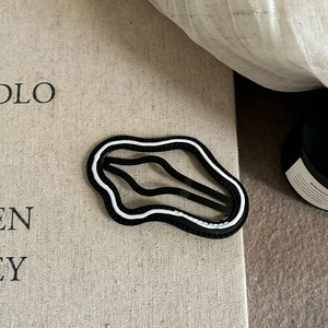Detailed view of wave-shaped black and white hair clip on minimalist aesthetic background