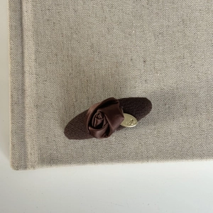 Detail of a brown fabric hair clip with a handmade satin rose and a golden metal logo plaque