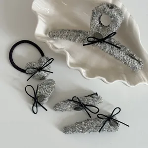 Dettaglio di fermagli per capelli in tweed grigio con fiocchi neri e ciondoli su piatto bianco