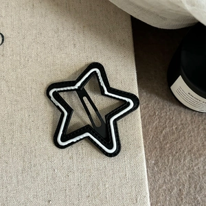 Star-shaped black and white BB hair clip placed on a textured beige linen background