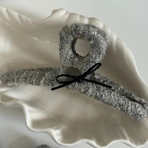 Pinza per capelli in tweed grigio con fiocco nero e placca metallica su vassoio shell