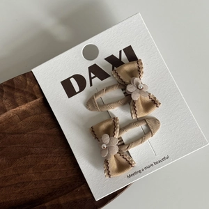 Détail de deux pinces à cheveux à nœud marron avec perles sur carte de présentation