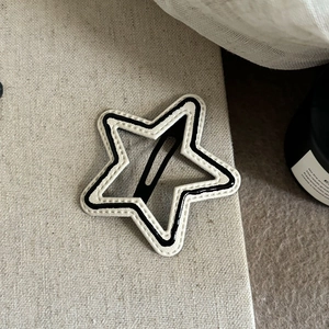 Star-shaped cream hair clip with black piping and sheer mesh detail on beige fabric