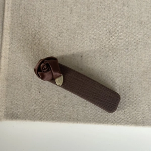 Detail of a brown fabric hair clip featuring a satin rose and small golden metal tag