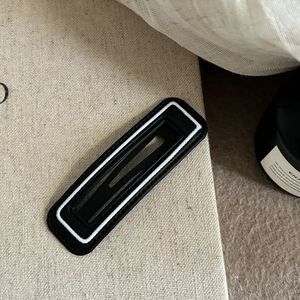 Minimalist black rectangular hair clip with white stripe on a beige textured background