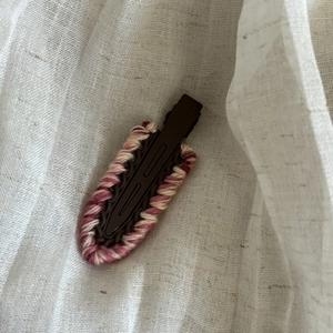 Pink and white knitted yarn hair clip with brown metal duckbill base on linen