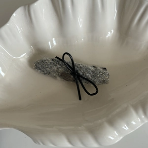 Dettaglio del fermaglio per capelli in tweed grigio con fiocco nero e placca in metallo