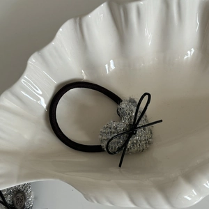 Dettaglio dell'elastico per capelli a cuore in tweed grigio con fiocco nero